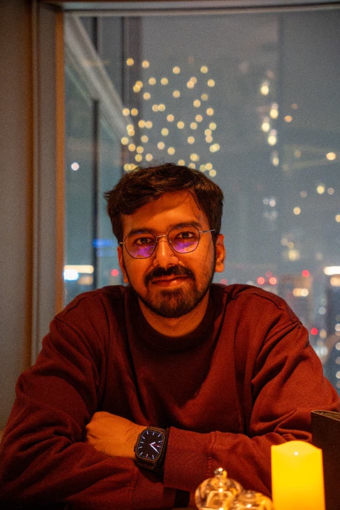 Pranav Jain seated by a window with a bokeh city skyline behind him